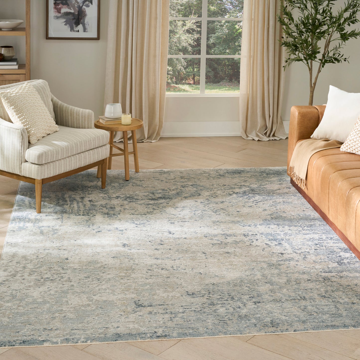Cozy living room with blue-gray patterned rug, cream armchair, tan sofa, wooden side table, potted plant and beige curtains.