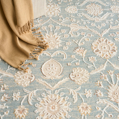 Light blue floral rug with ivory medallions and a beige fringed throw draped at the corner.