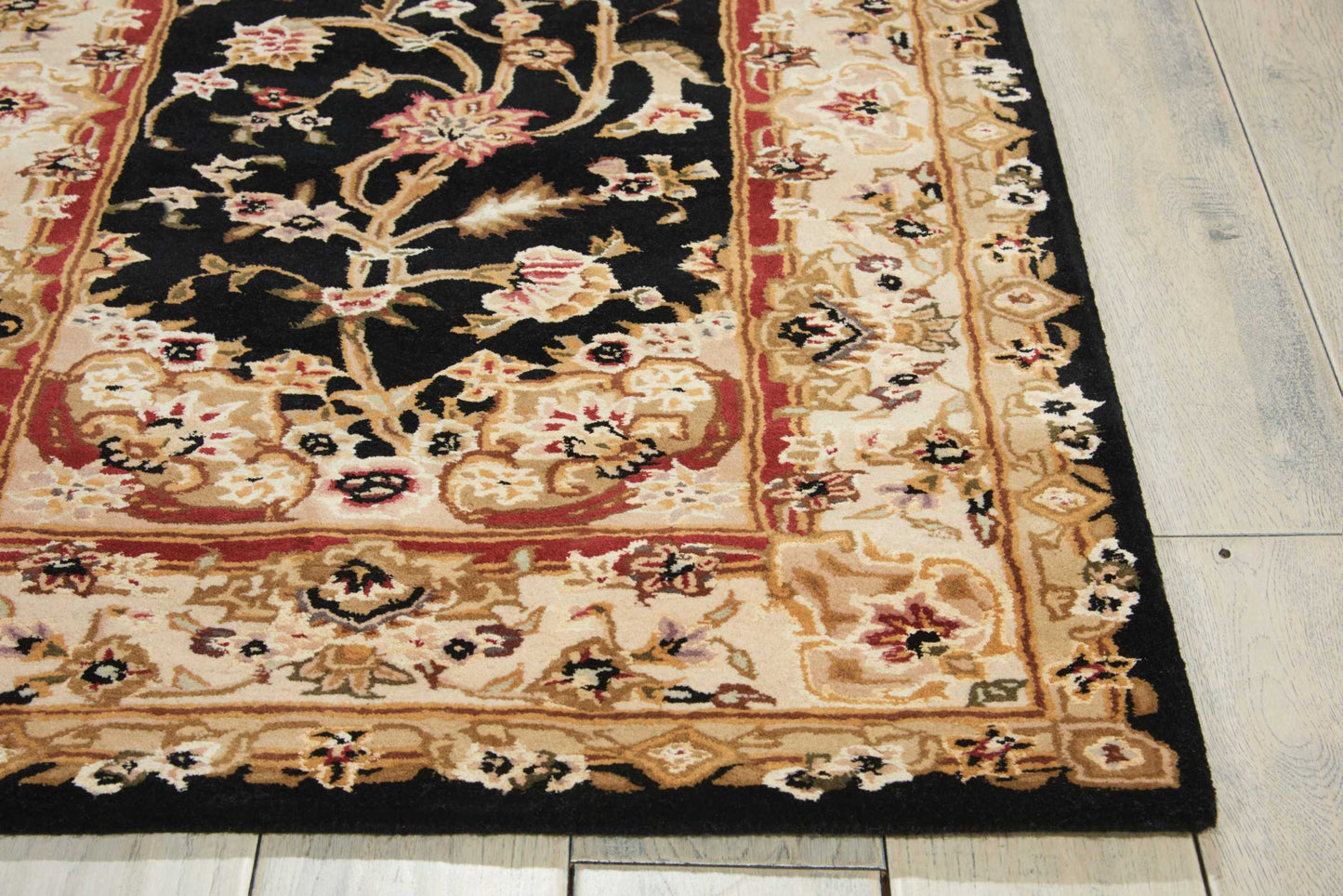 Rectangular oriental rug with black center, cream/beige floral border, red accents; floral vine motif, on wooden floor.