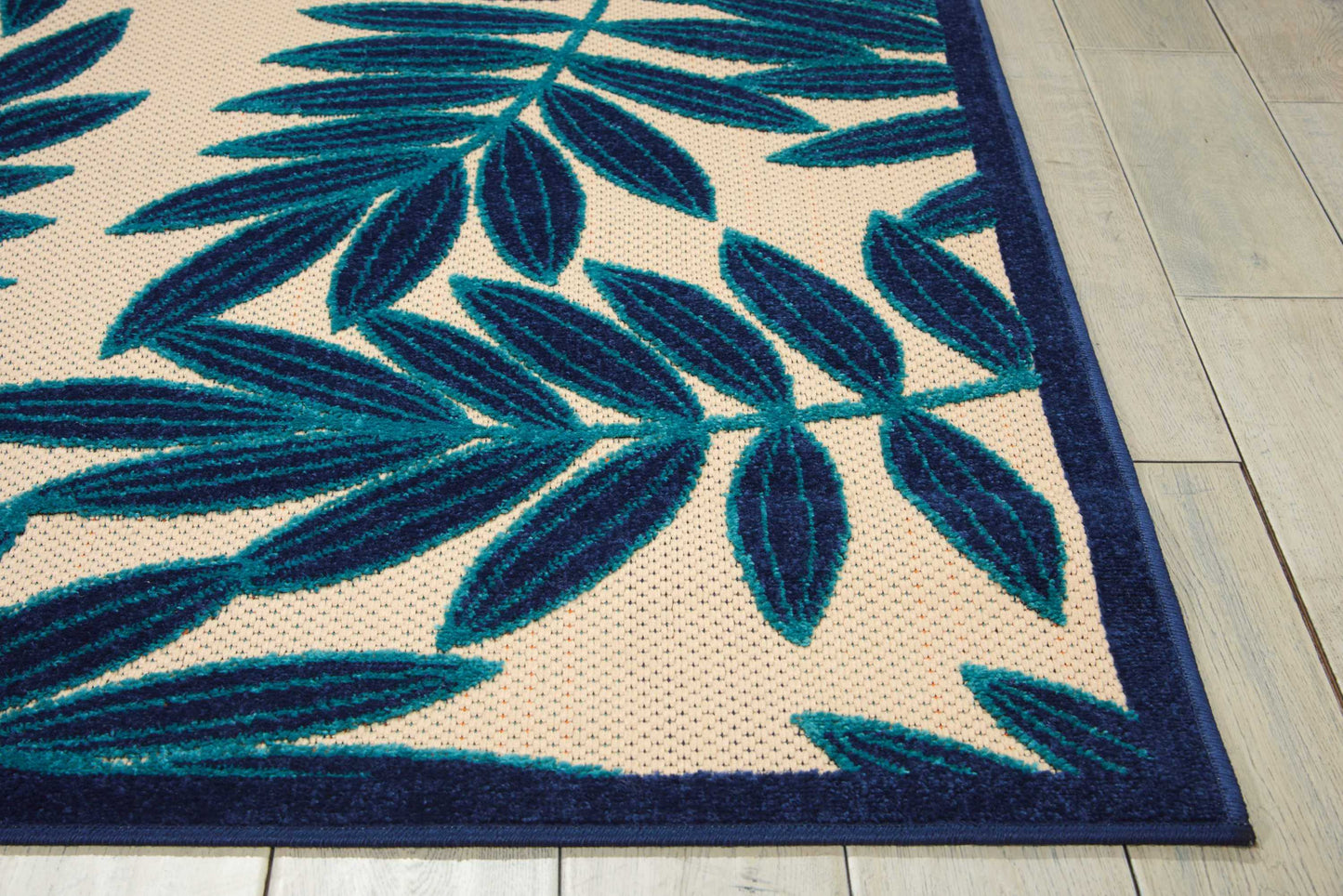 Beige woven area rug with teal-blue palm leaf pattern and dark navy border on wooden floor.