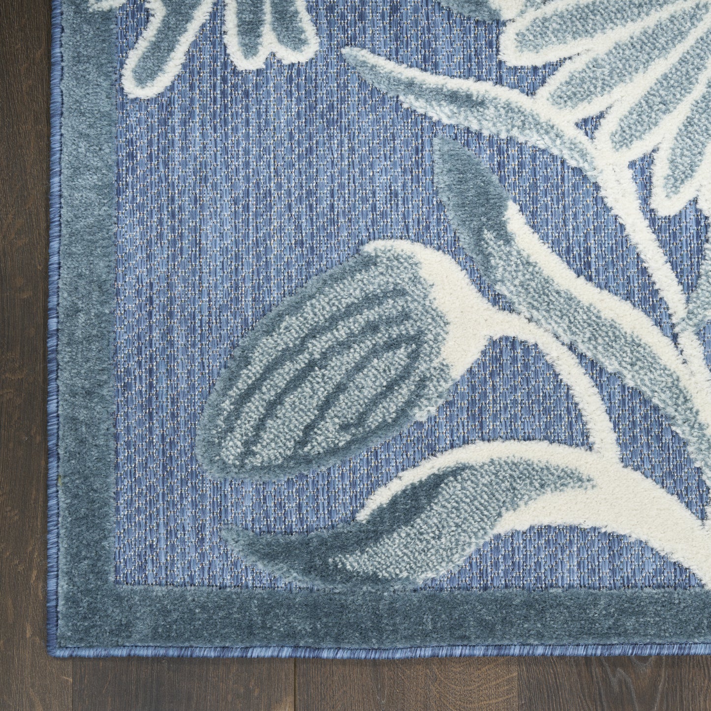 Blue rug with teal border and botanical leaf pattern in gray-blue and white, plush textured runner on wood floor.