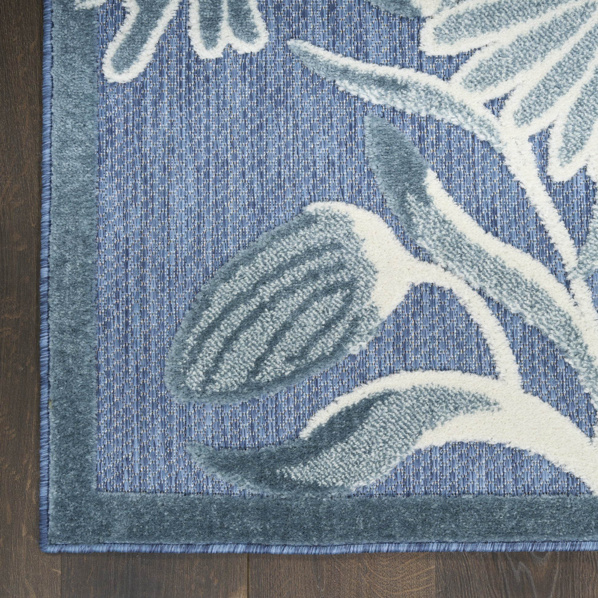 Blue rug with teal border and botanical leaf pattern in gray-blue and white, plush textured runner on wood floor.