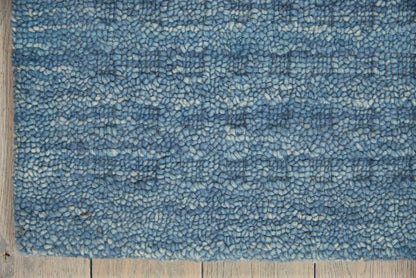 Blue shag rug with dense loop pile in variegated blues on a wooden floor.