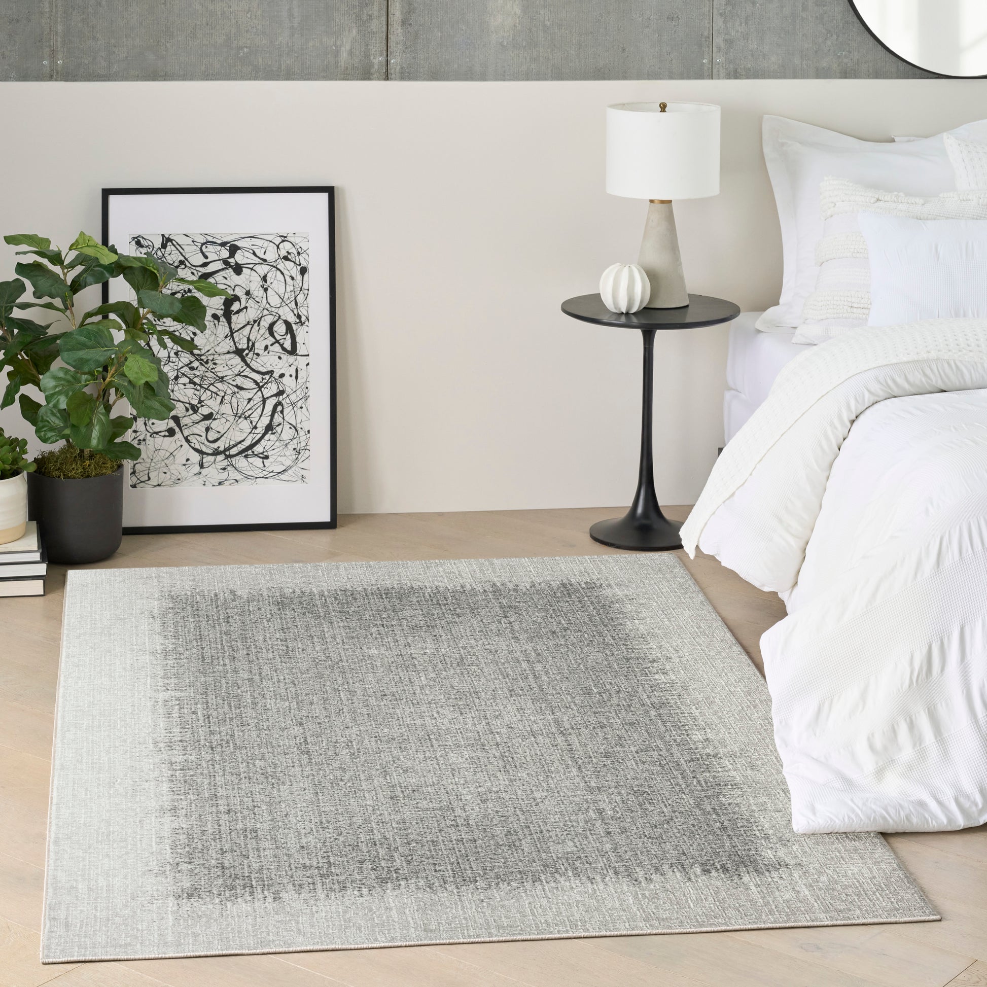 Rectangular light gray rug with a darker center gradient in a modern bedroom beside a white bed and a black side table.