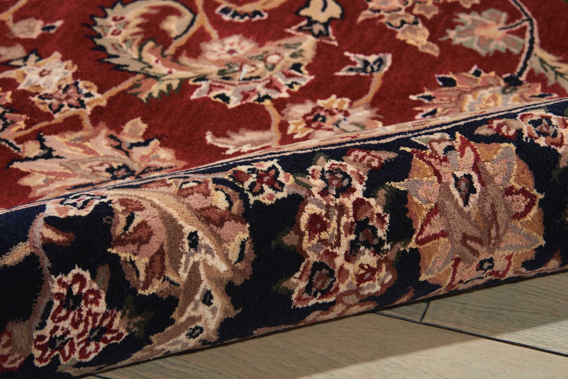 Round oriental wool rug with red field and cream floral motifs, navy border; rolled edge on wood floor.