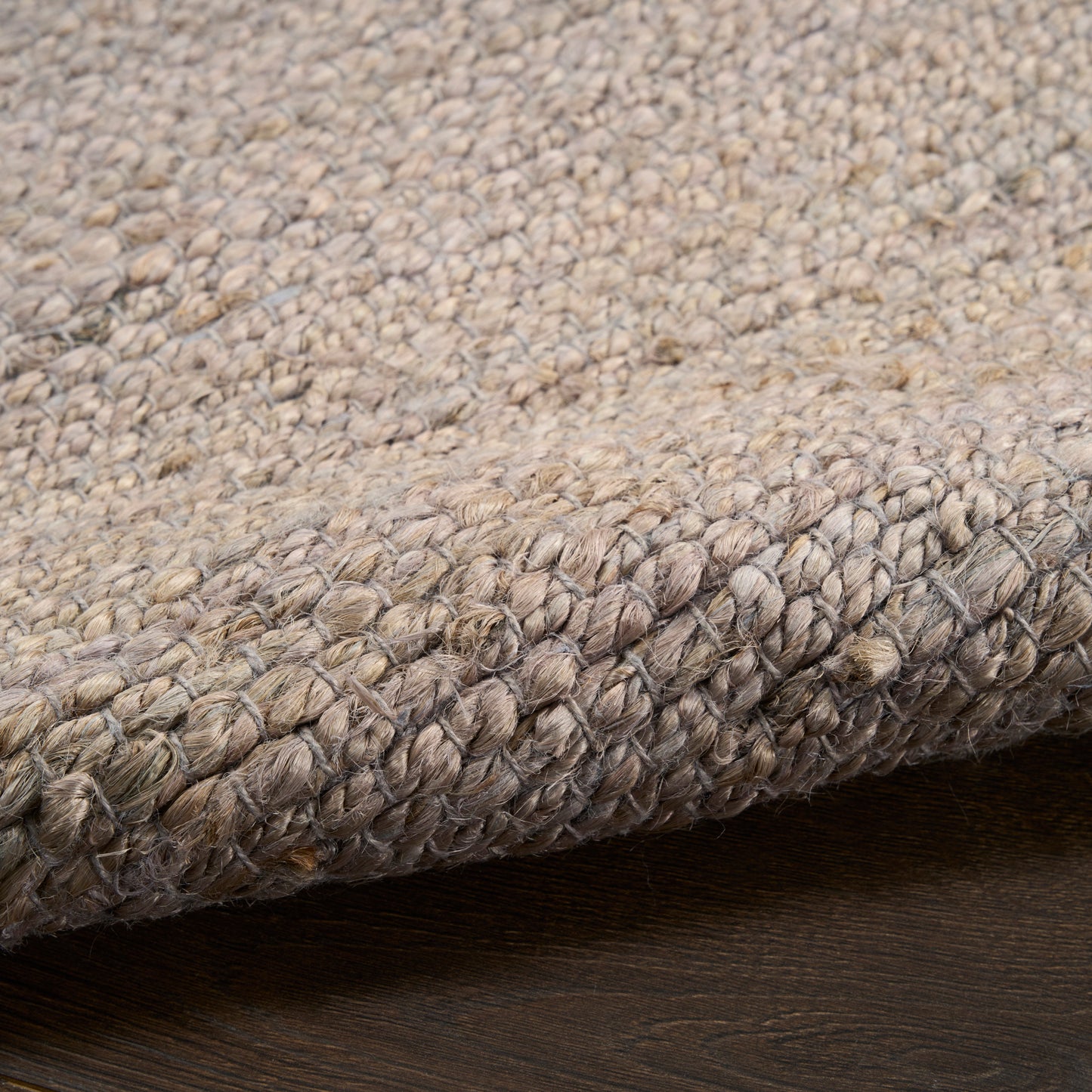 Beige-taupe looped wool rug close-up with dense textured weave and folded edge on dark wood floor.