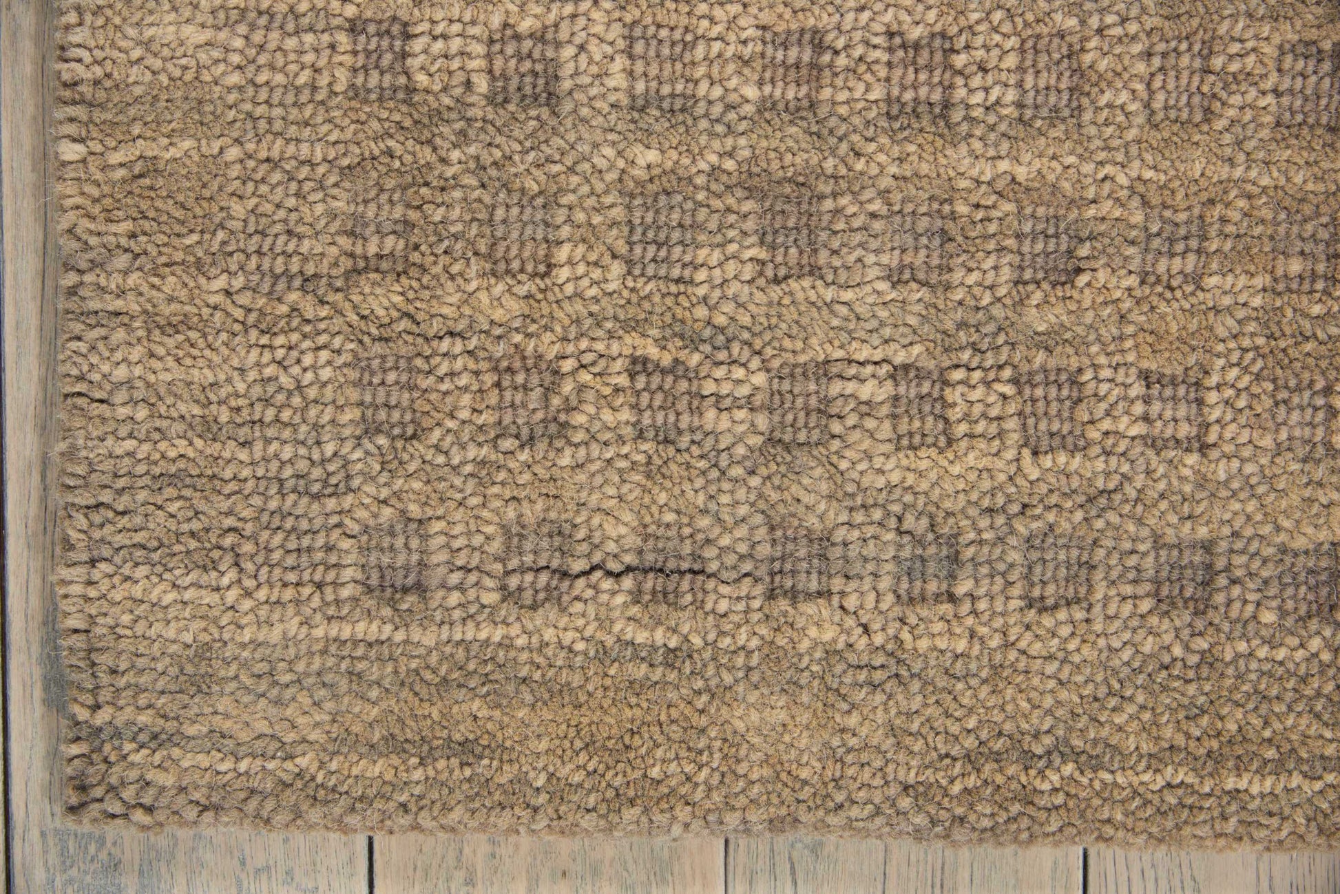 Beige shag rug with subtle geometric lattice pattern in taupe, plush pile, placed on weathered light wood floor.