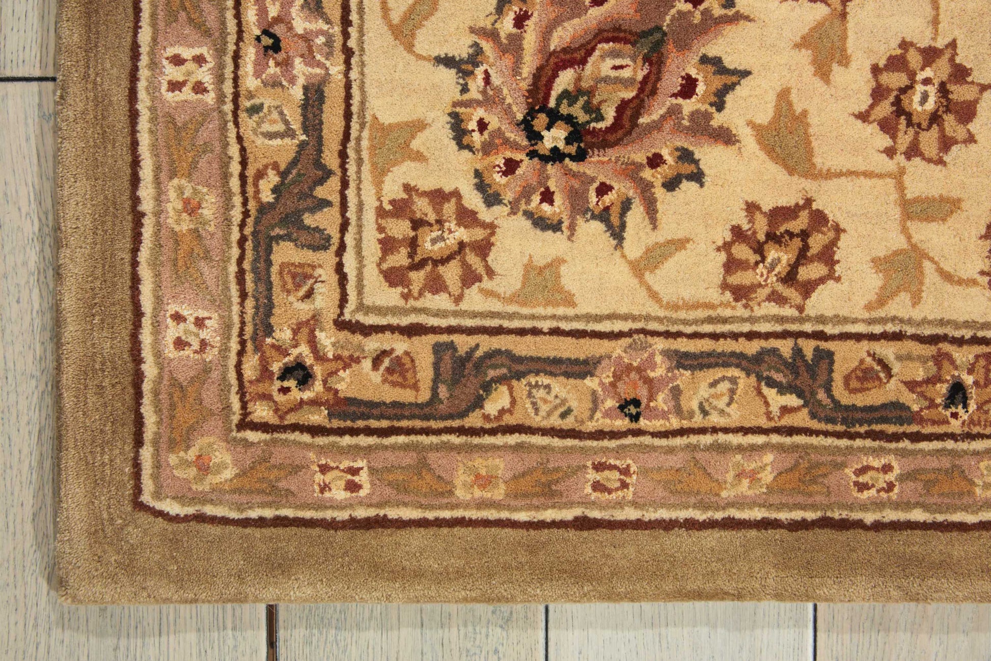 Beige floral area rug with ornate border on light wooden floor; warm cream, pink and brown tones.