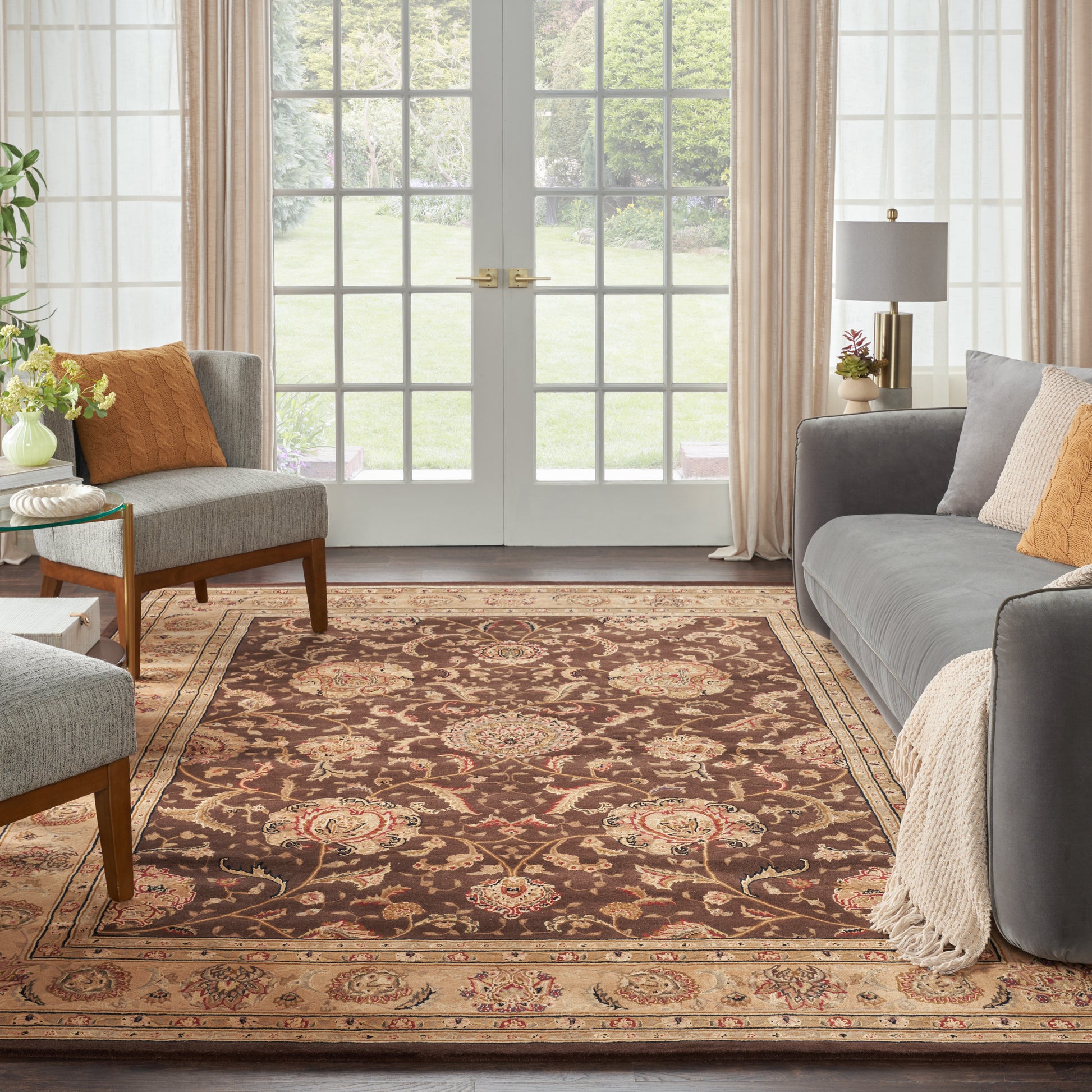 Classic living room with brown oriental rug, gray sofas, orange cushions, beige throw, and French doors with sheer curtains.