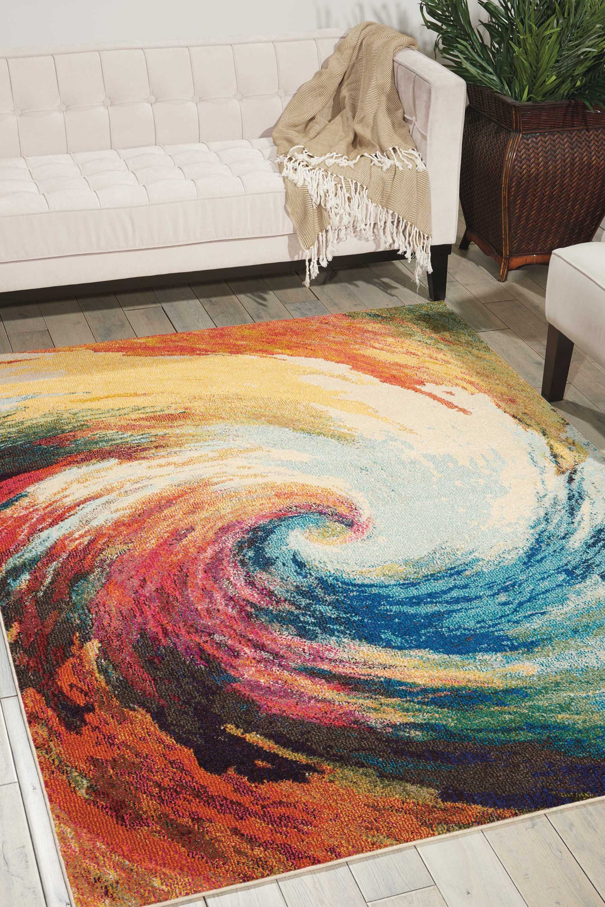 Rectangular rainbow swirl area rug in a modern living room with cream tufted sofa, beige fringed throw, and potted plant.
