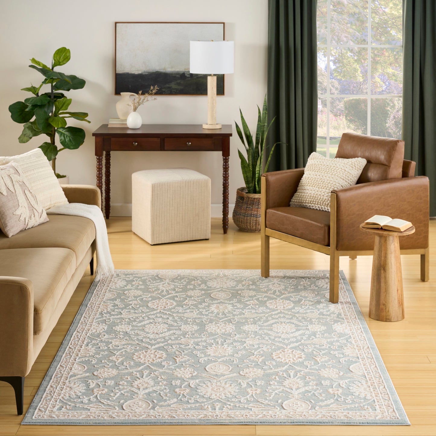 Cozy living room with beige sofa, brown leather armchair, blue floral rug, wooden console table, lamp, potted plants, and green-curtained window.