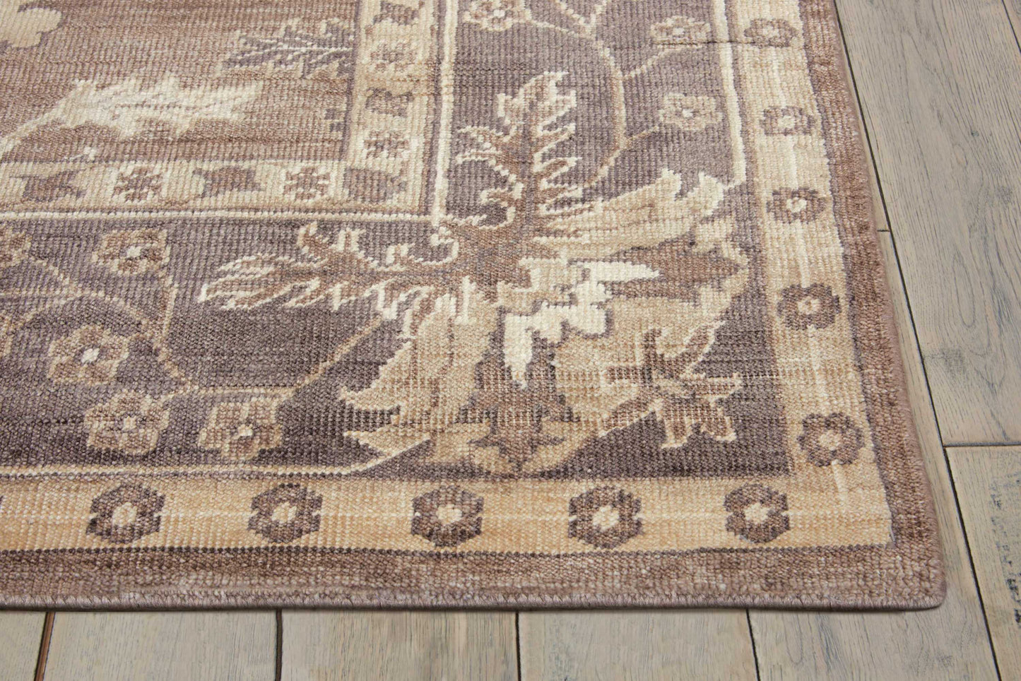 Beige-brown oriental rug with a large floral motif and decorative border on a wooden floor.