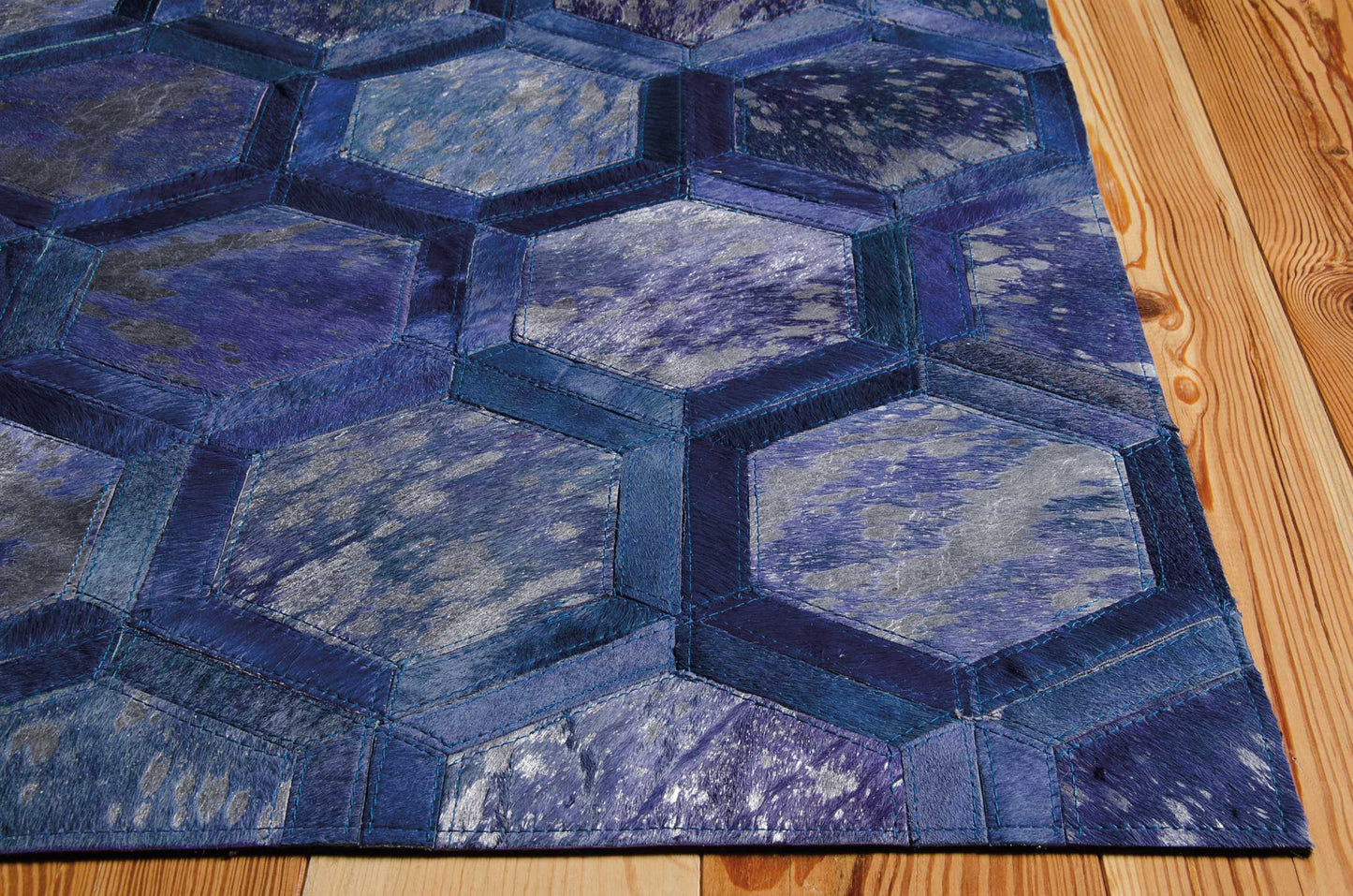 Blue hexagon patchwork rug with dark navy borders and lighter blue center panels on wooden floor.