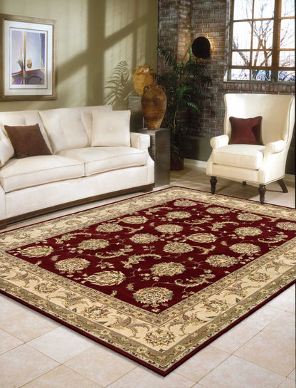 Ornate burgundy area rug with gold floral motifs and beige border in a cream living room with sofa and armchair.