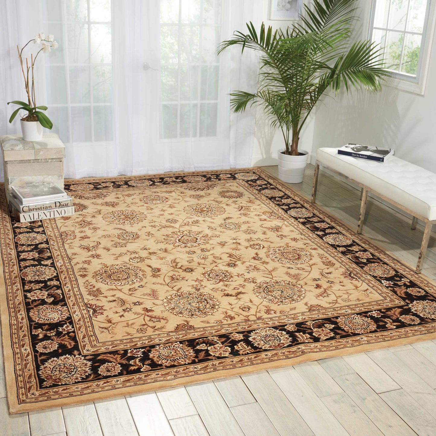 Rectangular beige oriental area rug with cream, brown & red medallions and a black floral border, in a bright living room.