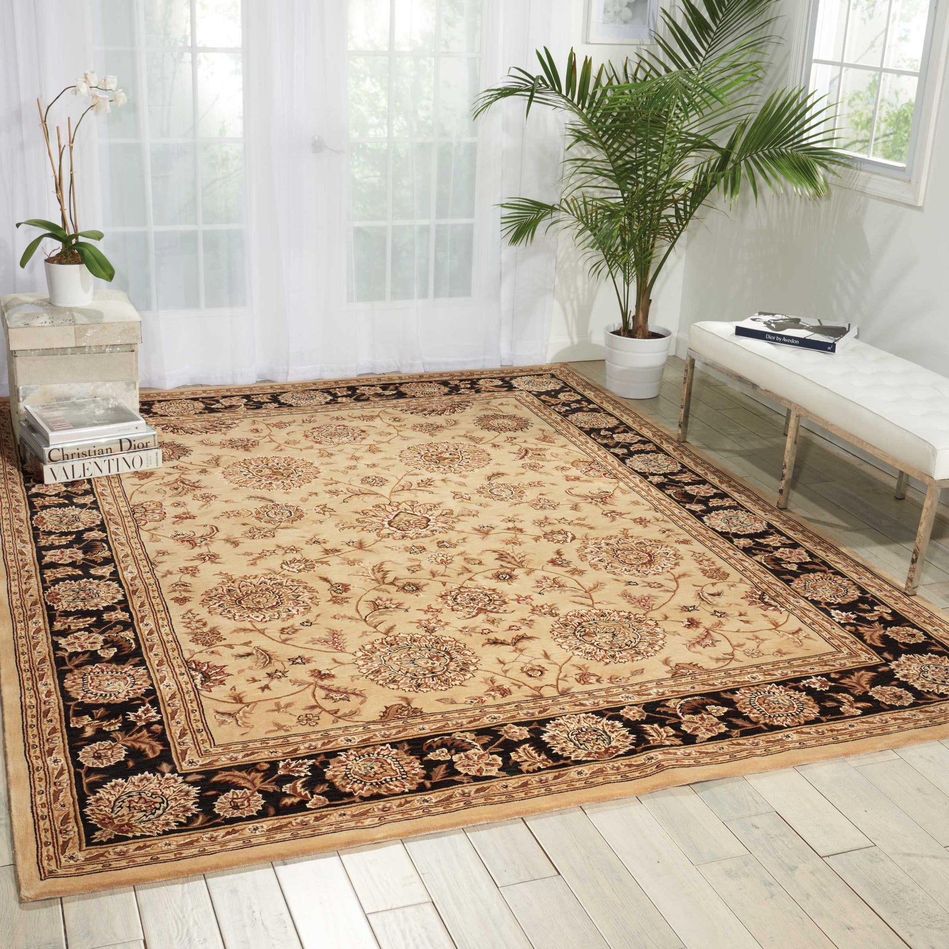 Rectangular beige oriental area rug with cream, brown & red medallions and a black floral border, in a bright living room.