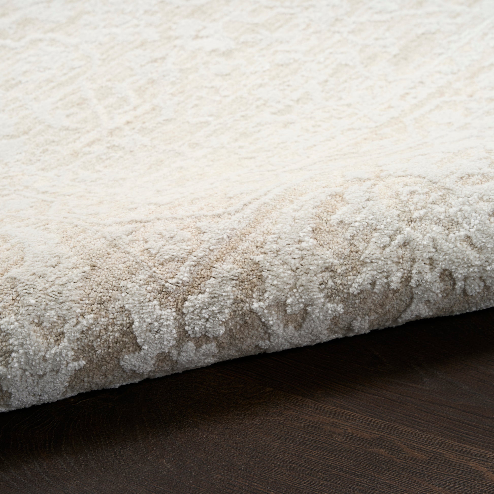 Cream textured area rug with plush pile and subtle pattern, rolled edge on dark wooden floor.