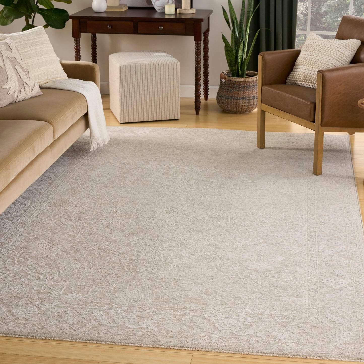 Light gray patterned area rug in a modern living room with beige sofa, brown armchair, wood furniture, and plants.