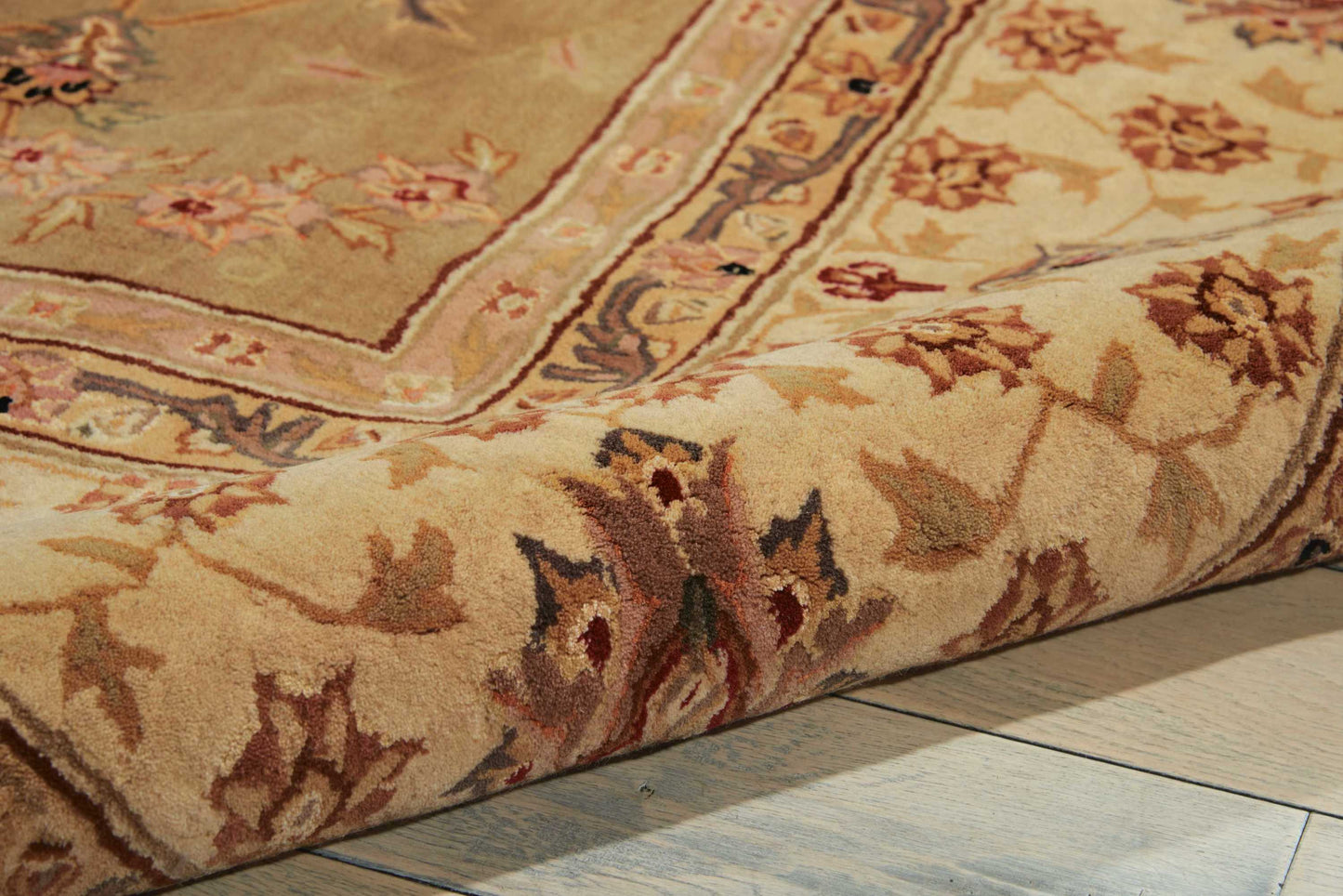 Beige oriental rug with ornate floral border; textured pile resting on light wooden floor.
