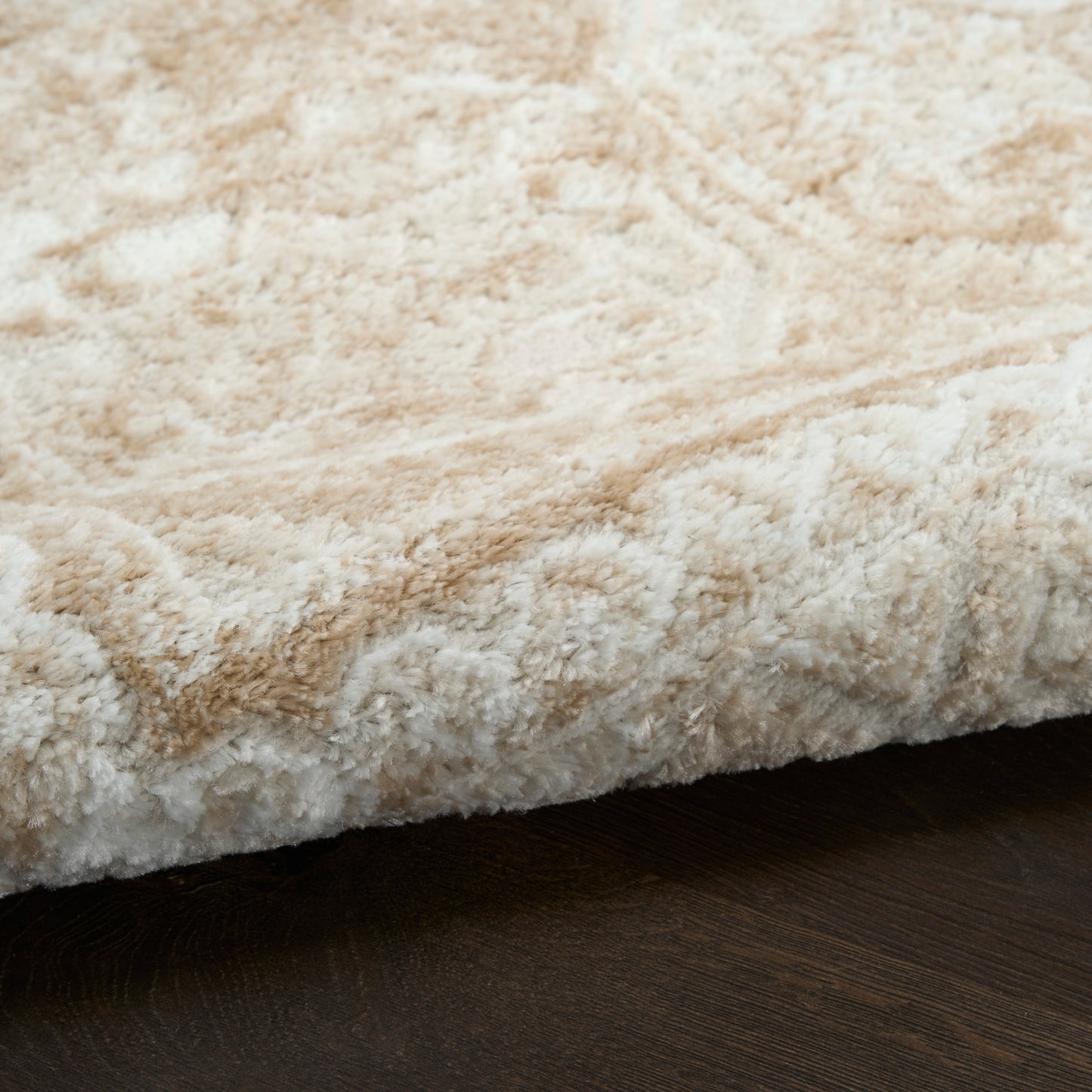 Beige cream shag rug close-up with fluffy pile and folded edge on dark wood floor.