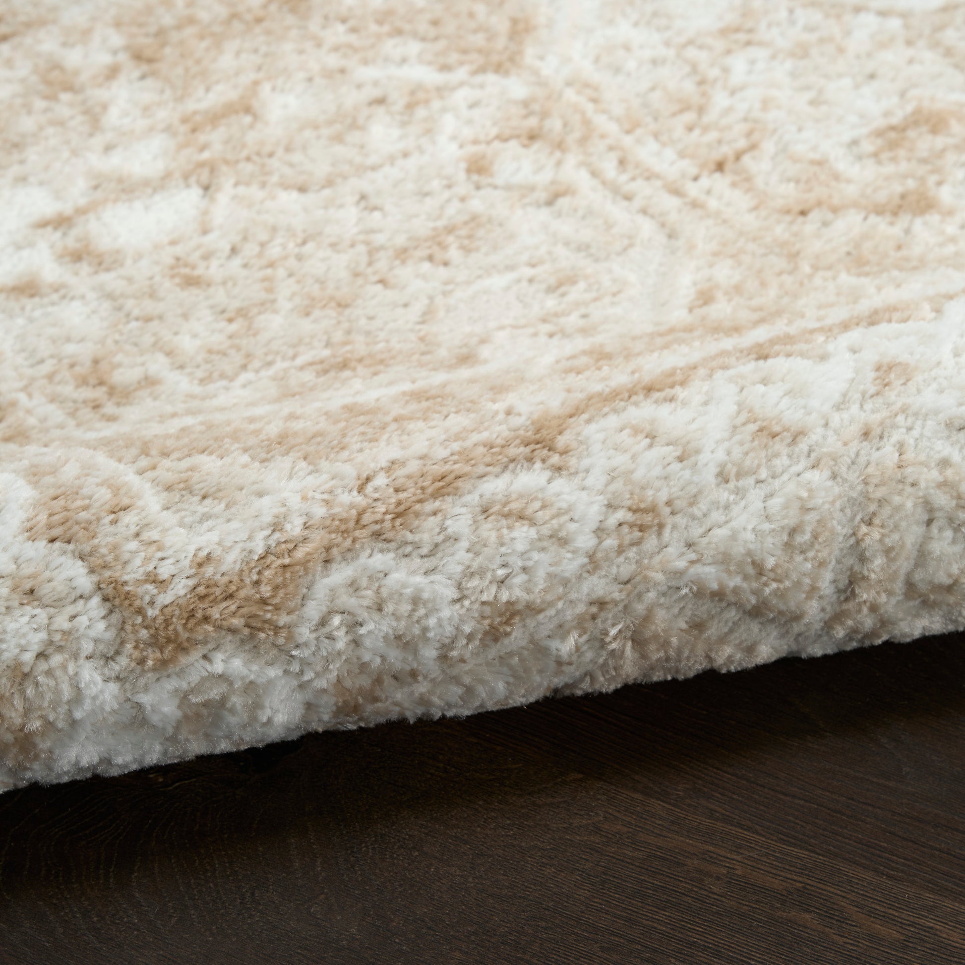 Beige cream shag rug close-up with fluffy pile and folded edge on dark wood floor.