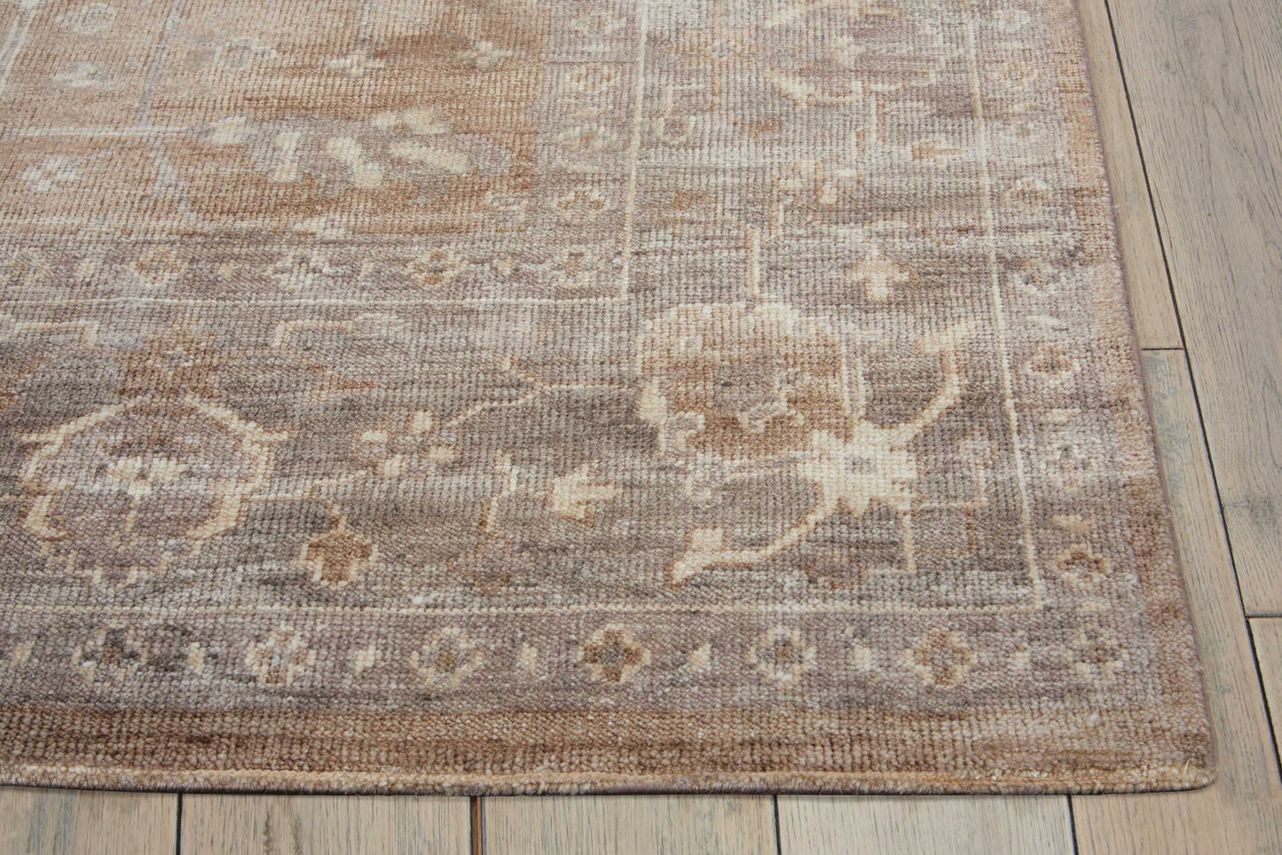Muted floral oriental area rug with beige, taupe and brown tones, medallion motifs and decorative border on a wooden floor.