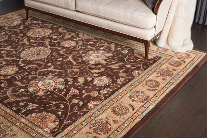 Oriental area rug with dark brown field, cream-gold border and floral motifs, under a beige sofa on dark wood floor.