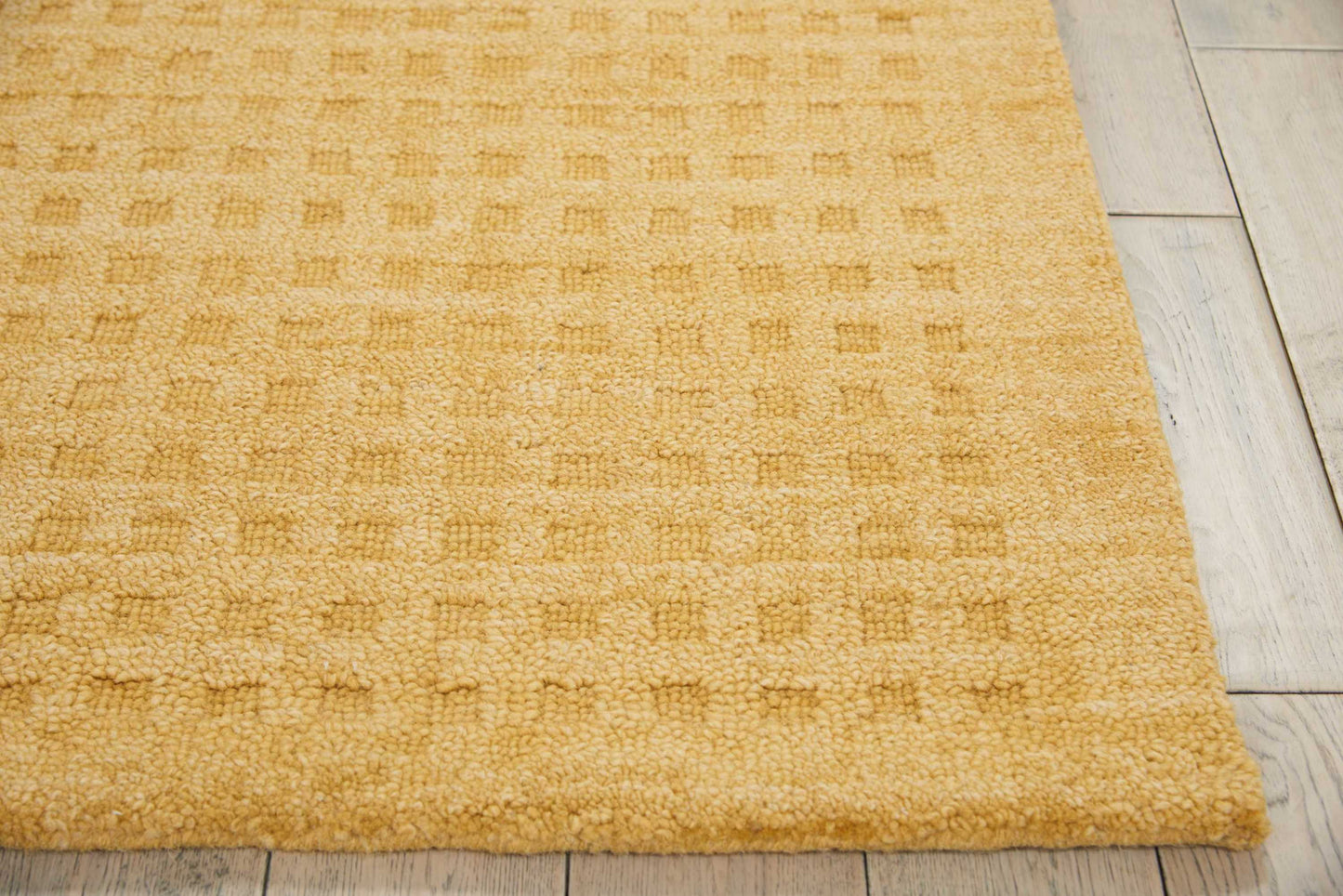 Mustard yellow textured loop-pile rug with subtle square pattern on light wood floor.