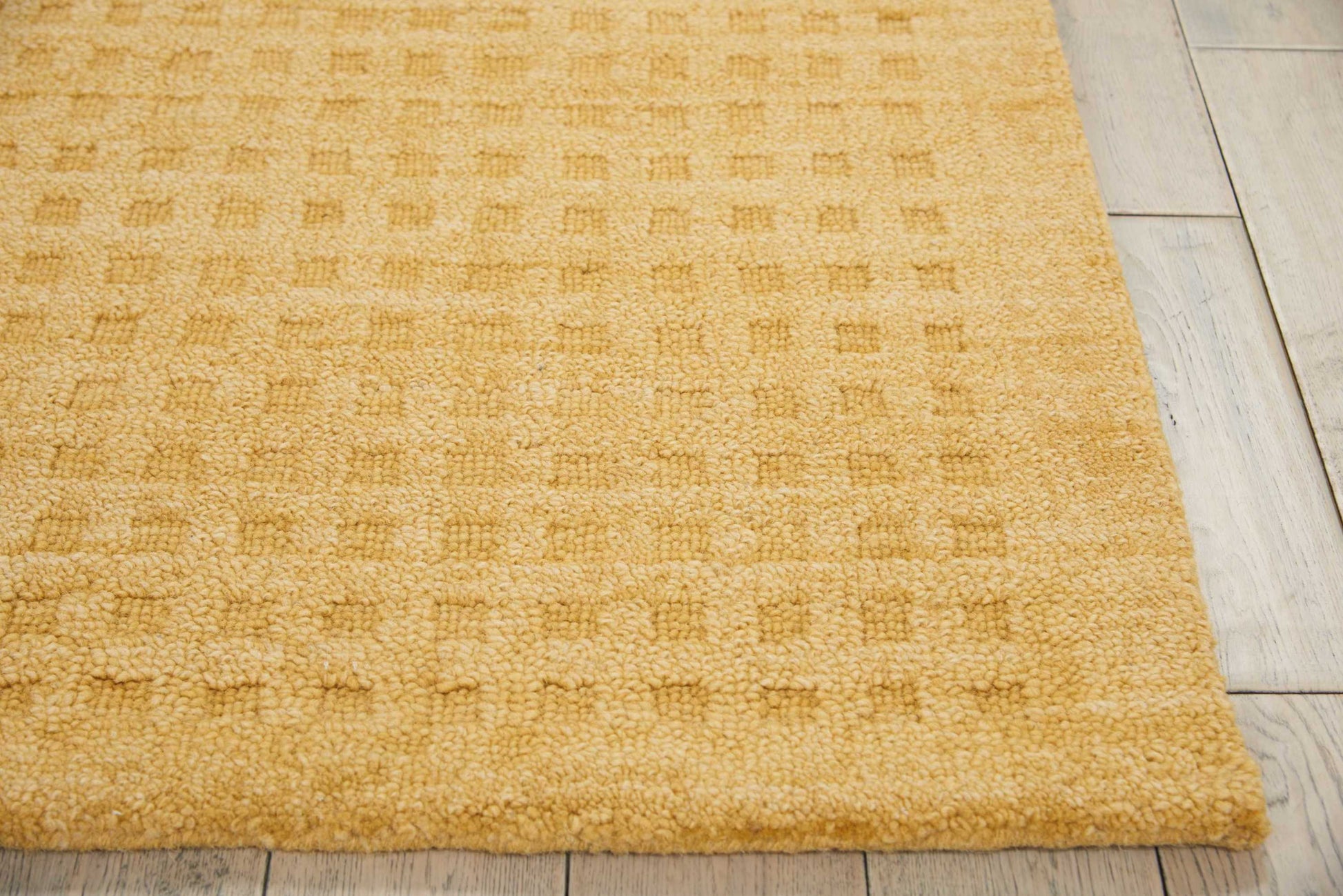 Mustard yellow textured loop-pile rug with subtle square pattern on light wood floor.