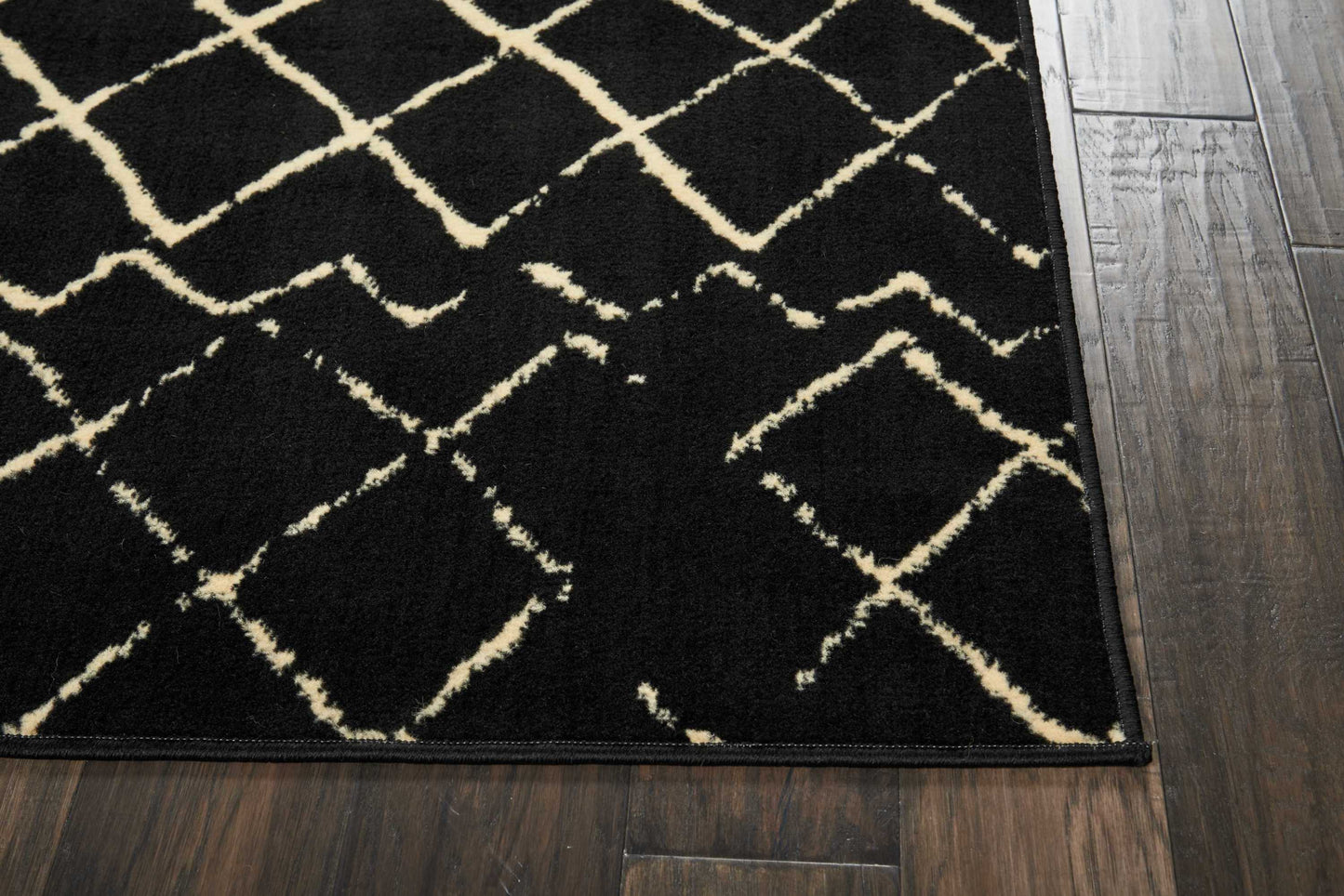 Black low-pile rug with cream geometric diamond lattice on dark wood floor.