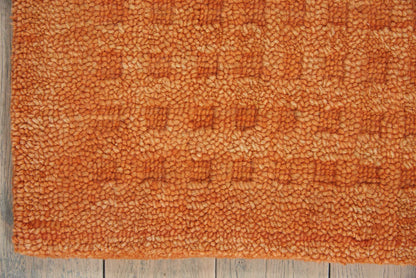 Orange shag rug on a weathered wood floor; plush, looped pile with a warm, textured look.