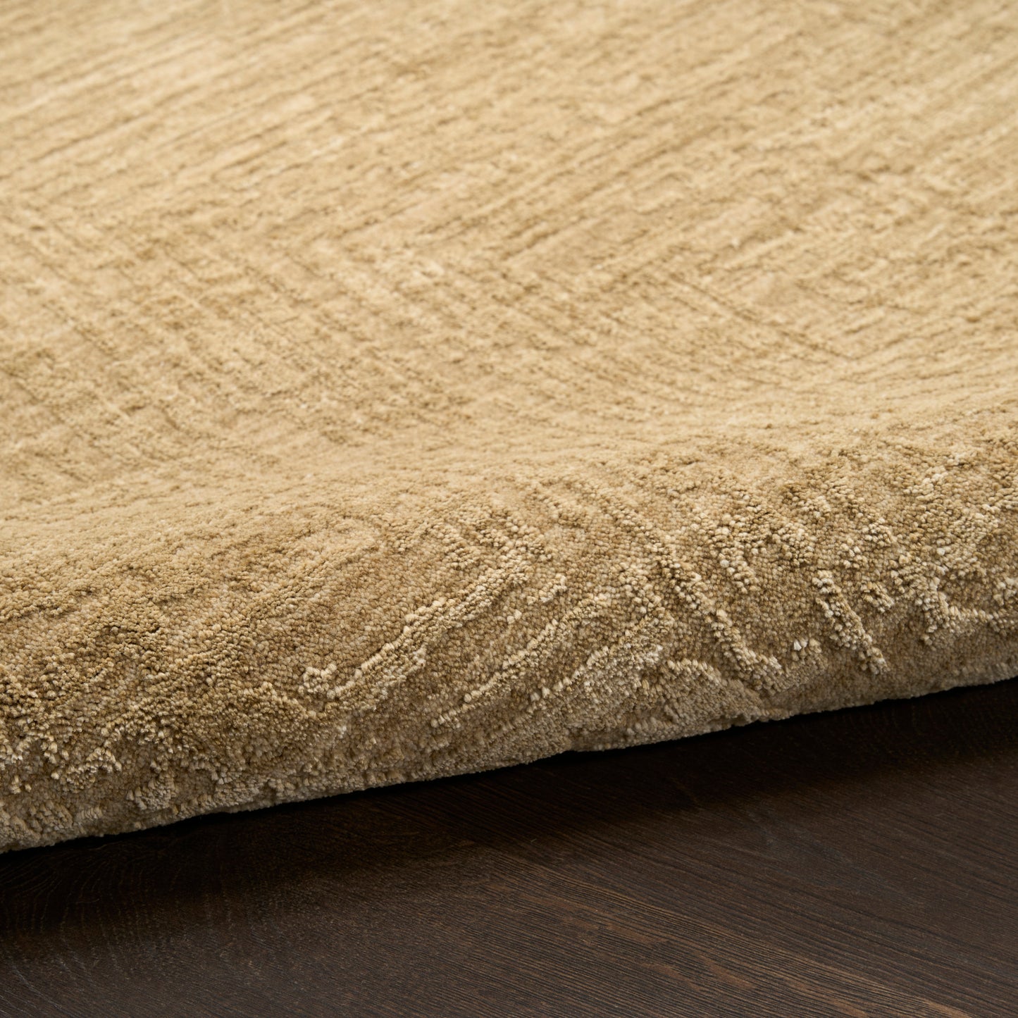 Beige textured rug with soft pile and rolled edge, woven pattern, on dark wood floor.