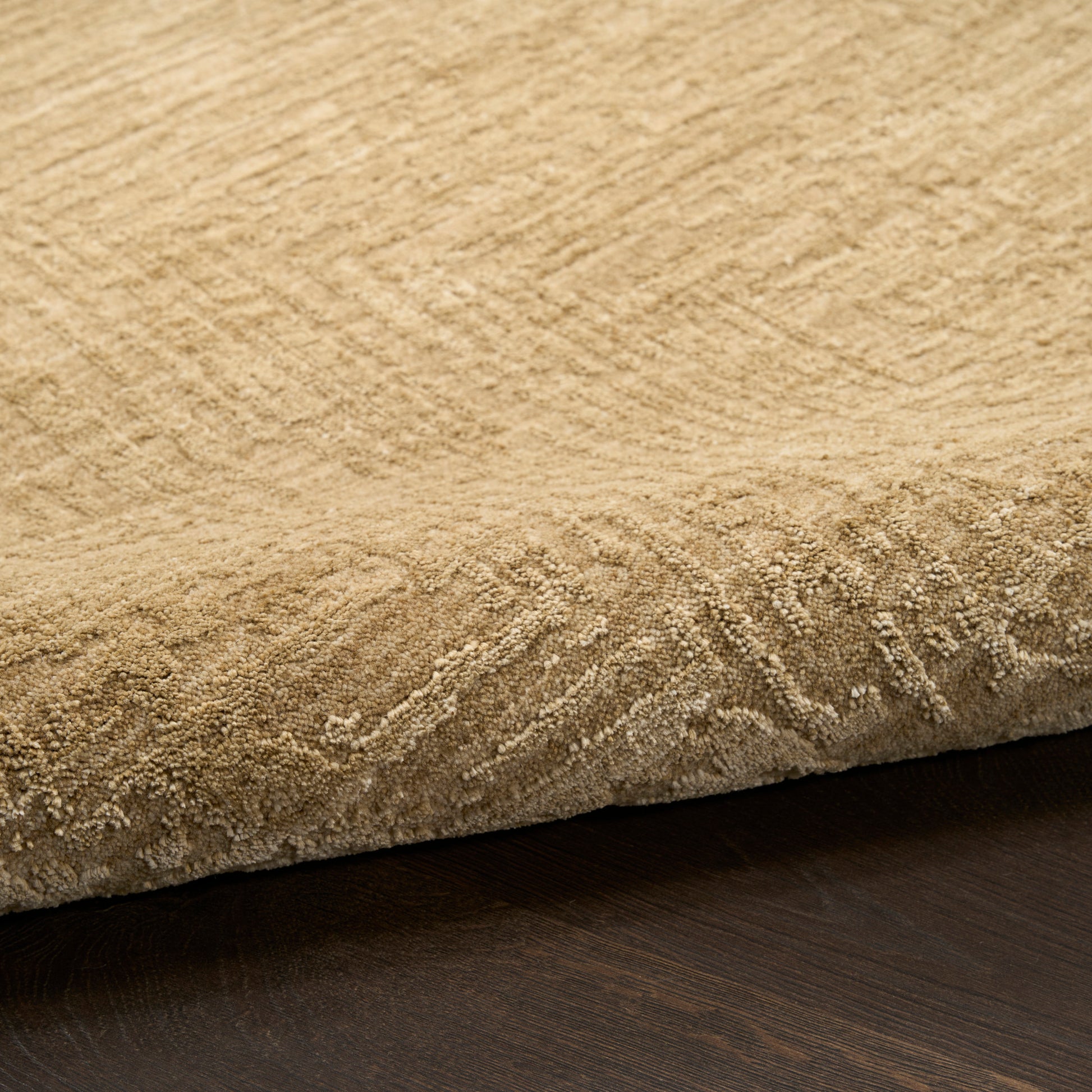 Beige textured rug with soft pile and rolled edge, woven pattern, on dark wood floor.