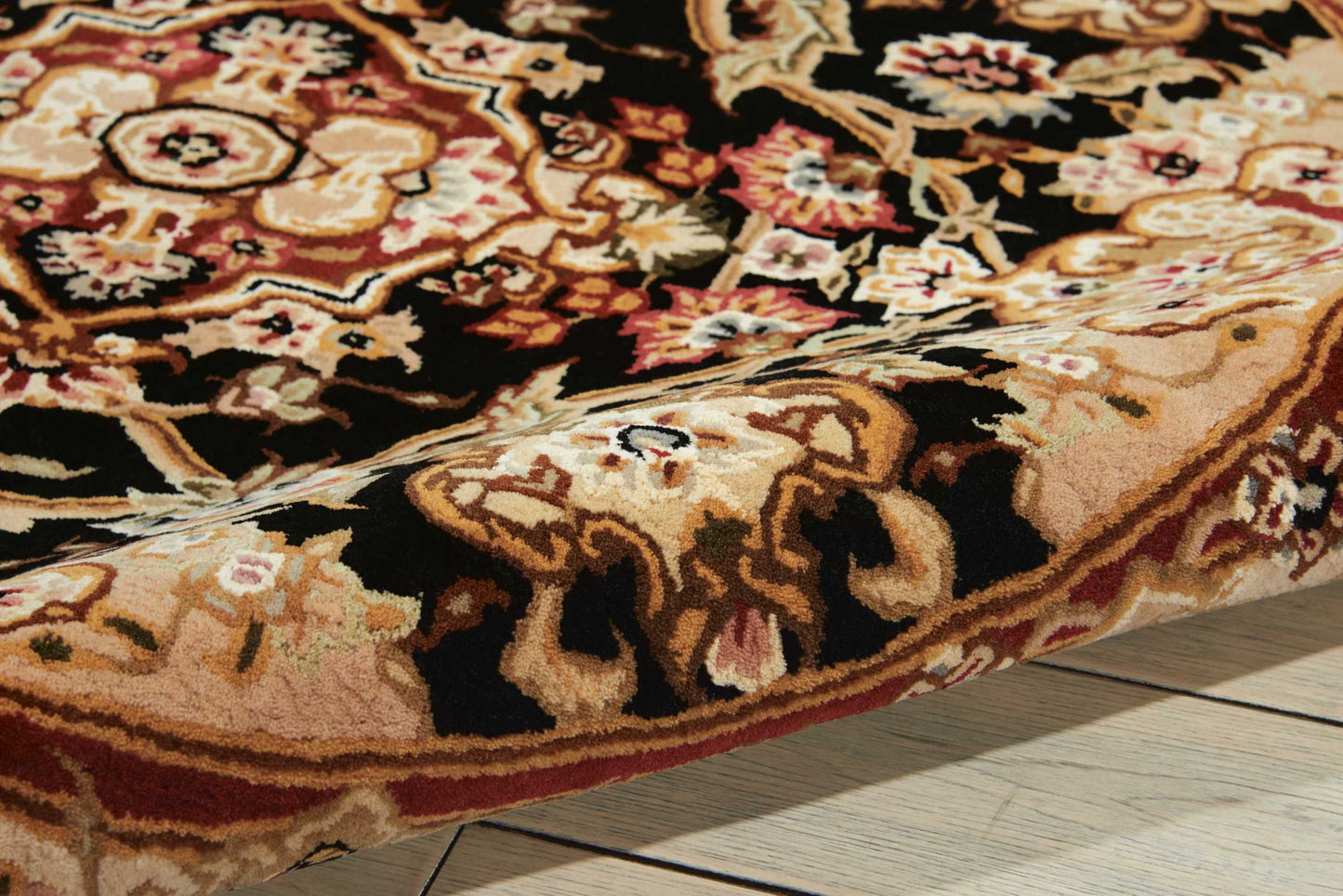 Close-up of a plush oriental rug with red, cream, and gold floral medallions and a folded edge on wood flooring.