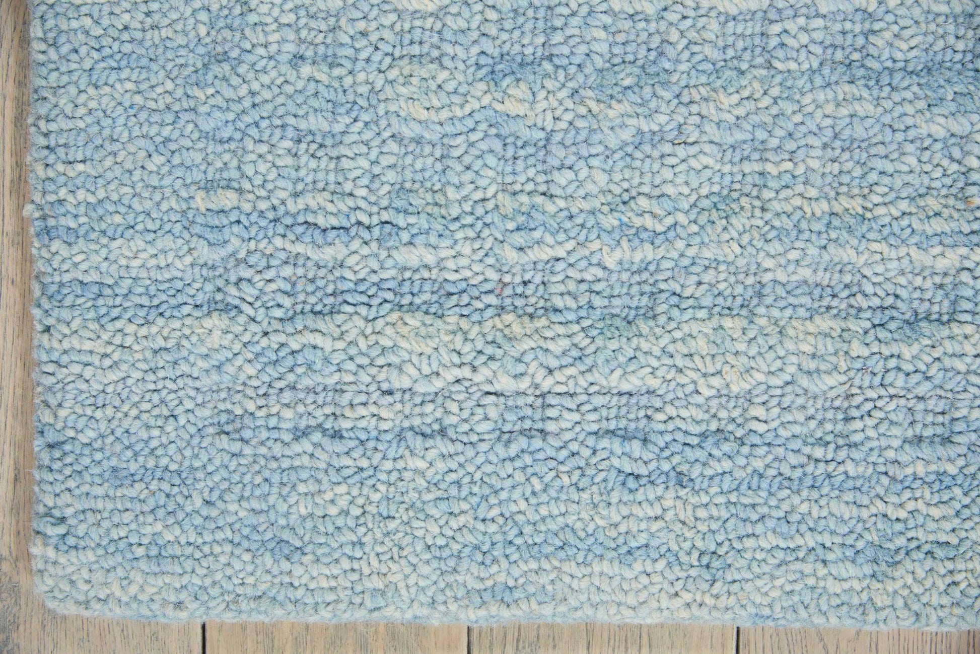 Blue shag rug with variegated light and medium blue tones and pale cream accents on a wooden floor.