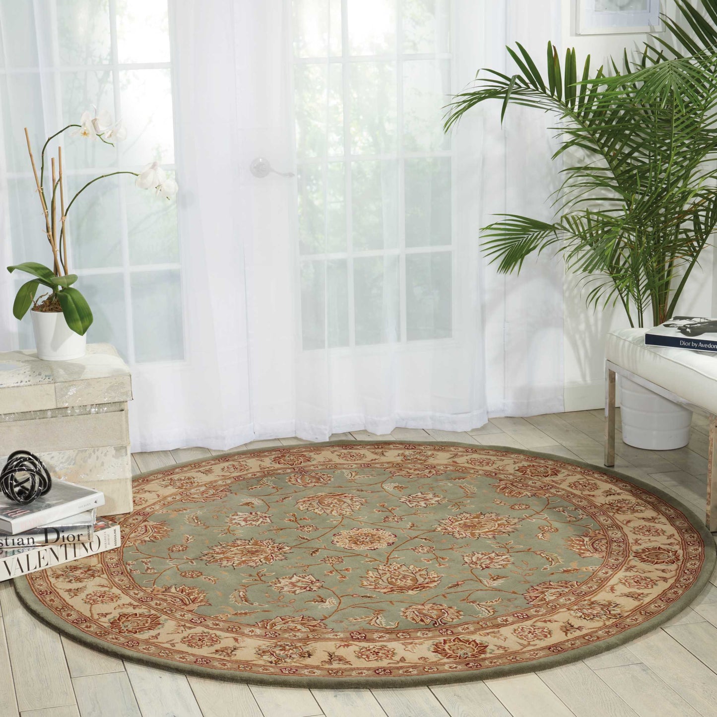 Round oriental rug with teal center and red-beige border, floral motif, in a bright living room with plants.