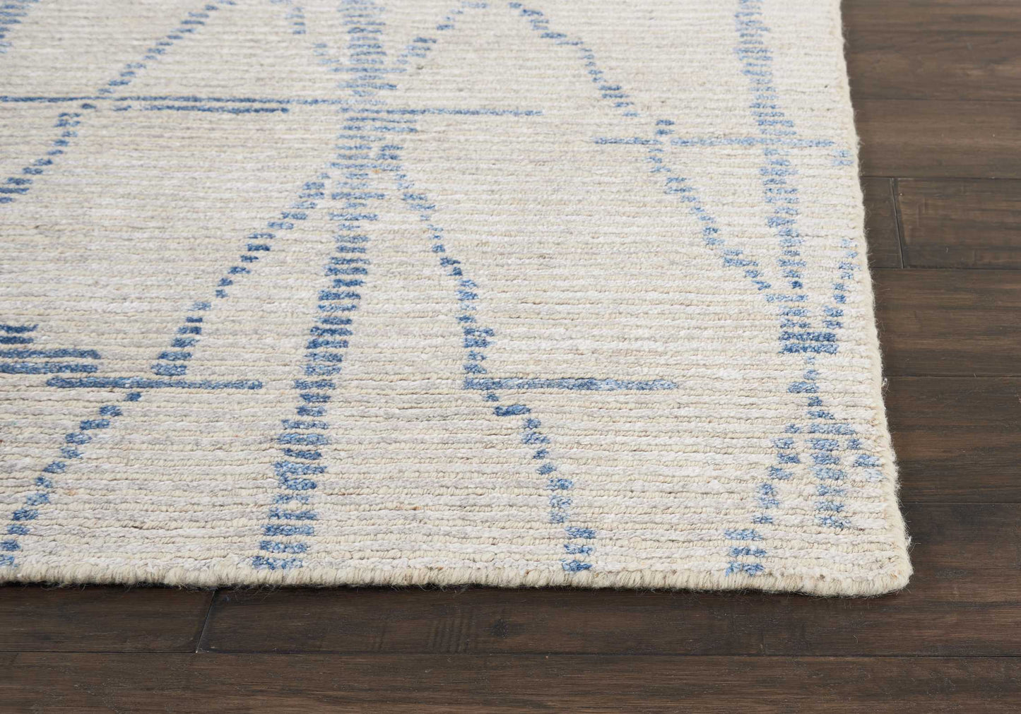 Cream rug with blue abstract geometric lines on dark wood floor; soft, low-pile textile.