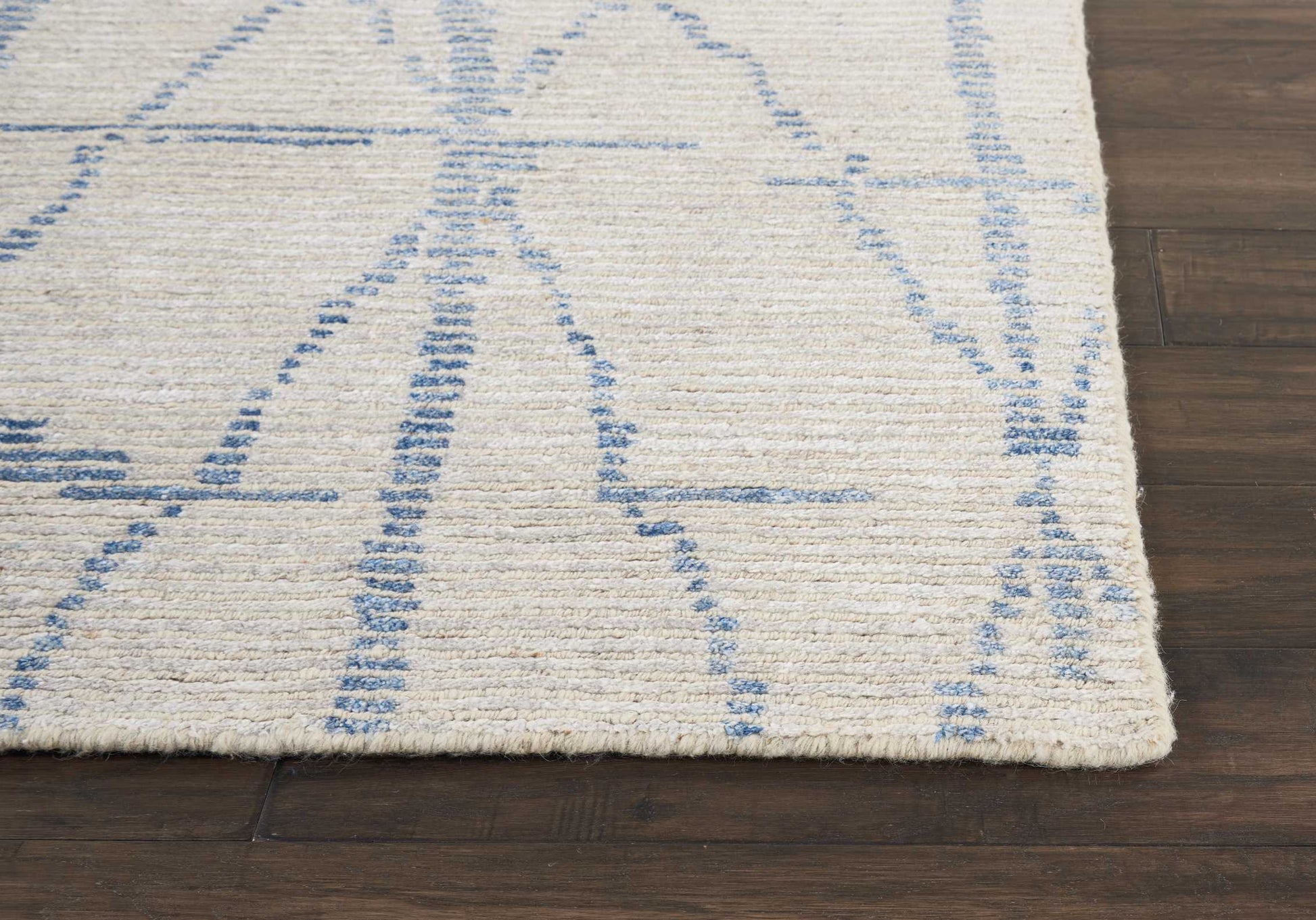 Cream rug with blue abstract geometric lines on dark wood floor; soft, low-pile textile.