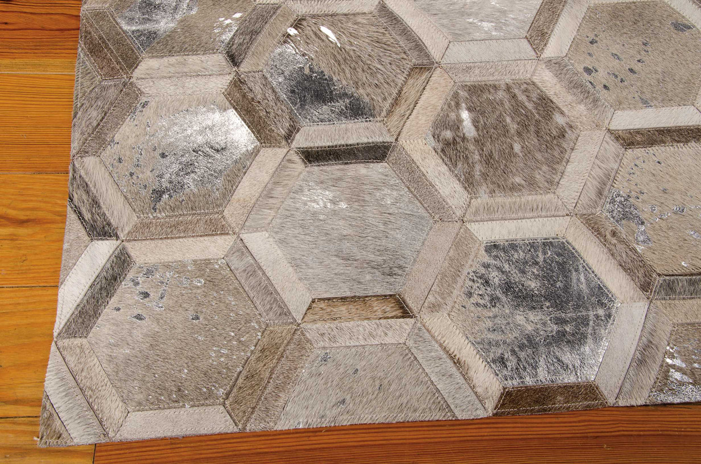 Geometric hexagon patchwork rug with subtle metallic sheen in gray, taupe and brown tones on wooden floor.