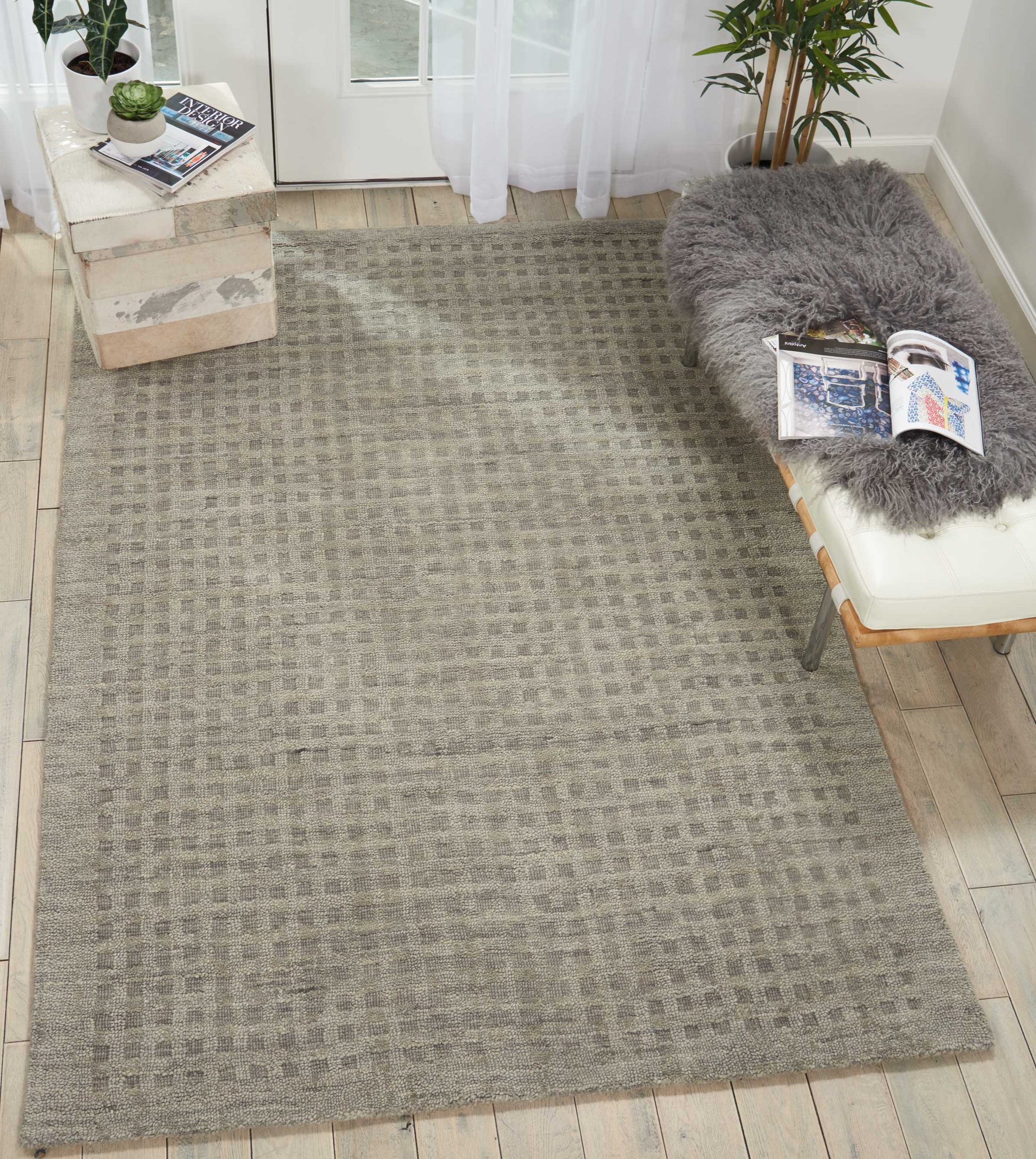 Light gray woven area rug with subtle checkered grid pattern on light wood flooring near a glass door.