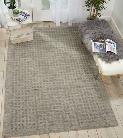 Light gray woven area rug with subtle checkered grid pattern on light wood flooring near a glass door.