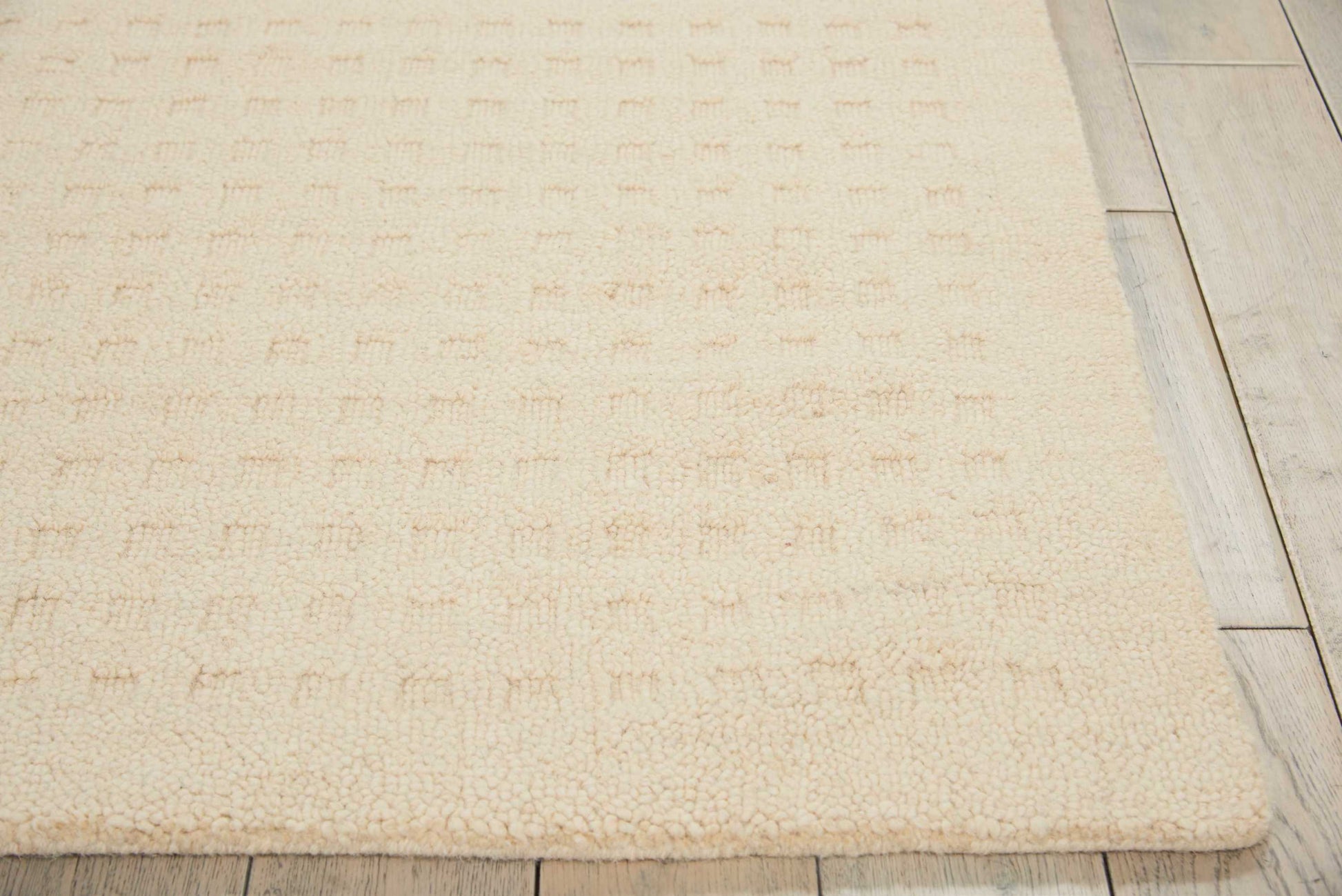 Beige shag rug with a subtle tufted grid texture on light wood floor.