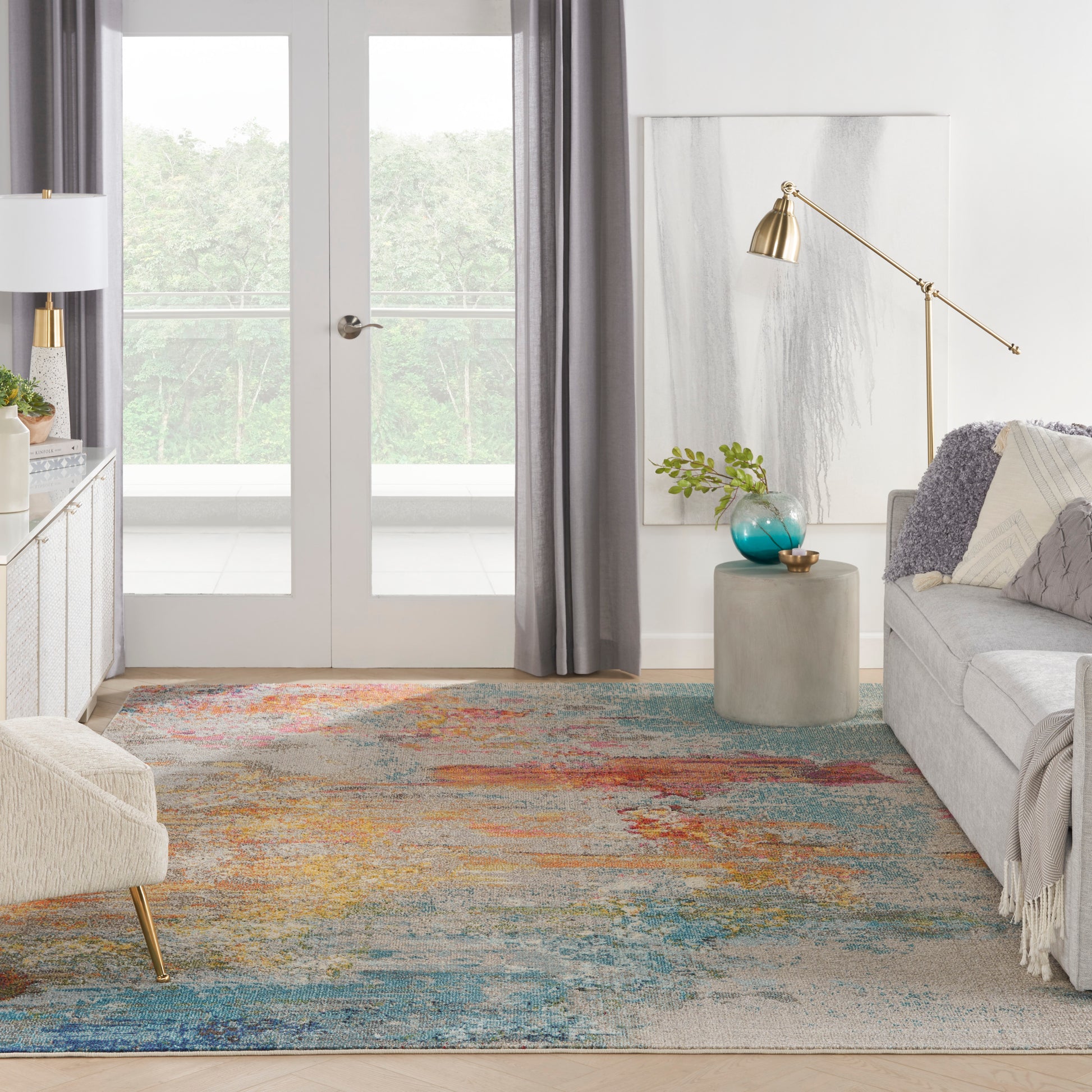 Modern living room with colorful rug, gray sofa, glass doors, gold arc floor lamp, concrete side table, turquoise vase.