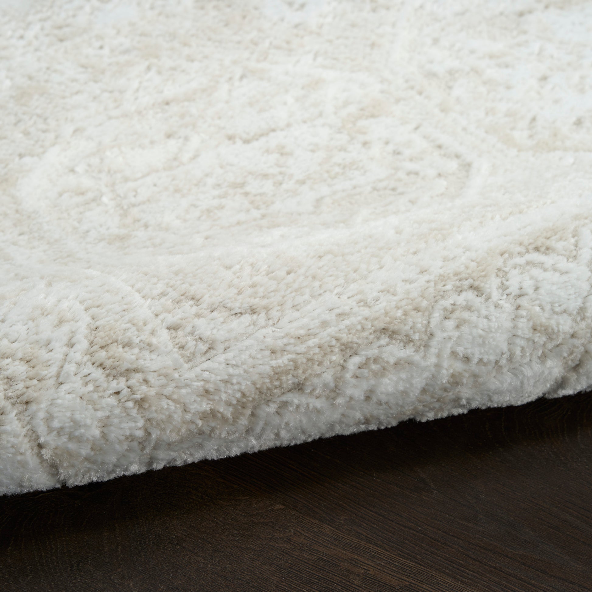 Cream fluffy shag rug with thick pile on dark wooden floor.