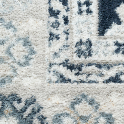 Close-up of a cream shag rug with blue-gray geometric medallion pattern and soft textured pile.