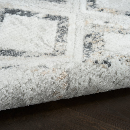 Thick white and gray geometric rug with subtle beige accents, plush shag pile, folded edge on dark wood floor.