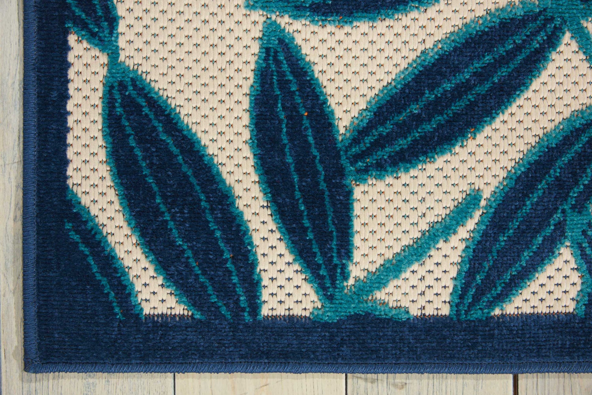 Teal leaf-motif rug with cream background and dark blue border; woven decorative area rug.