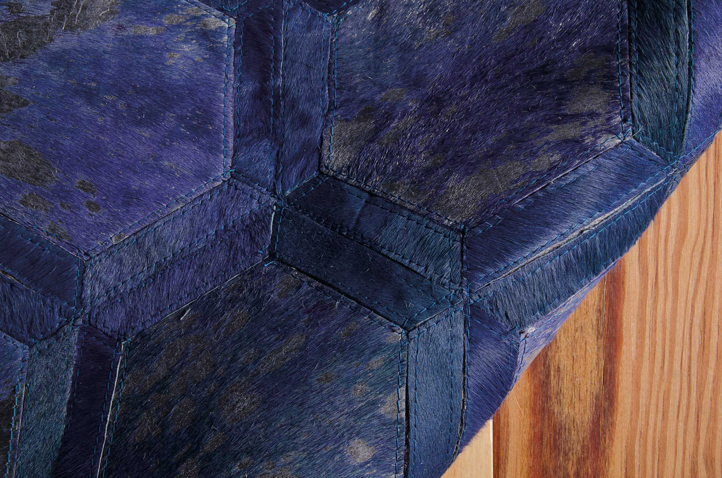Blue hexagon-patch quilted panels with teal stitching; fur-textured, close-up on wood floor.