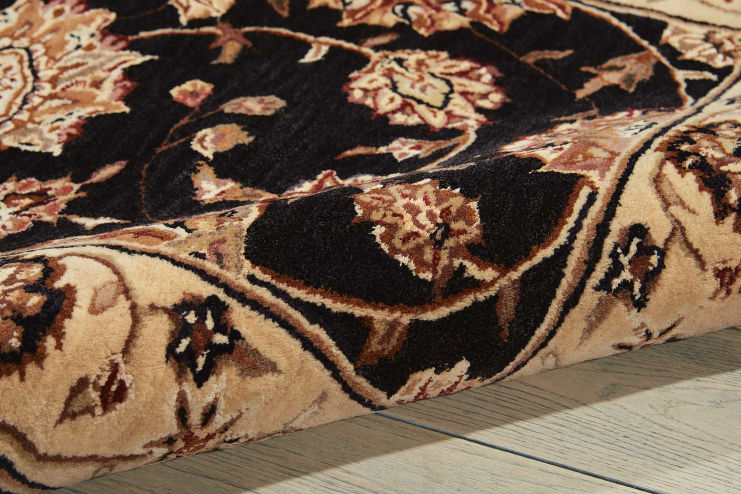 Close-up of a traditional floral oriental rug in black, beige and brown on a wooden floor.