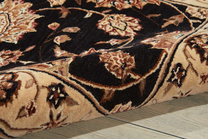 Close-up of a traditional floral oriental rug in black, beige and brown on a wooden floor.